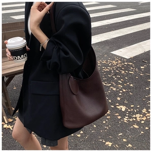 Detail of dark brown leather hobo bucket bag with a round charm shown in urban street setting
