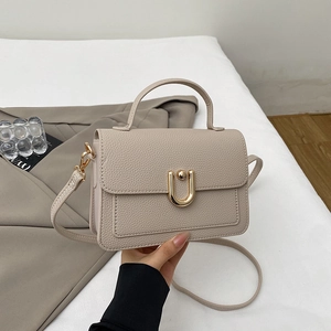 Close-up of golden U-shaped metal buckle and lychee pattern on off-white handbag