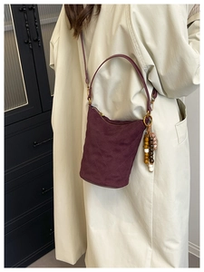Vue détaillée du sac seau matelassé bordeaux avec breloque en bois sur un trench-coat beige