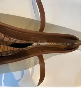 Close-up of smooth gold zipper closure and striped lining on the two-tone tote bag