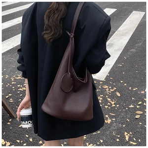 Detail of dark brown pebble leather bucket bag with knotted shoulder strap on a model