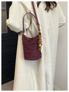 Détail du sac seau matelassé bordeaux avec pompon en perles sur manteau beige