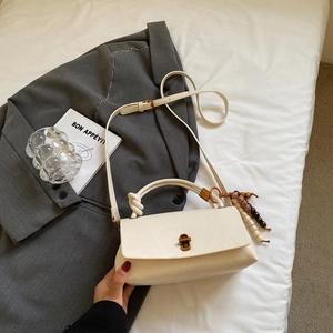 Detail view of cream white handbag featuring a knotted handle and beaded tassel charm