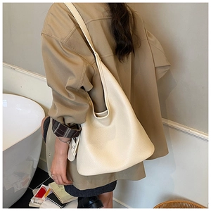 Chic cream bucket bag in lychee leather worn as a shoulder bag by a model