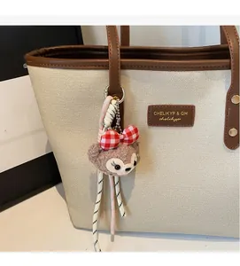 Detail view of cream tote bag featuring brown leather handles and a plush bear pendant