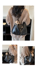Detail view of black vintage soft leather tote bag with a beige plush doll charm accessory