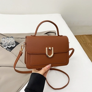 Detailed macro view of the brown lychee leather texture and U-shaped gold metal buckle
