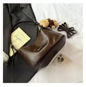 Detail of dark brown tote bag showing leather texture, metal tag, and plush bear charm