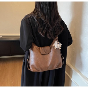 Close-up of vintage brown leather tote bag with round buckle and white plush charm
