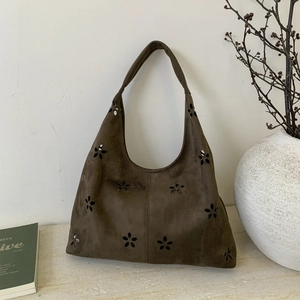 Detail of laser-cut floral pattern on a dark brown suede tote bag in a lifestyle setting