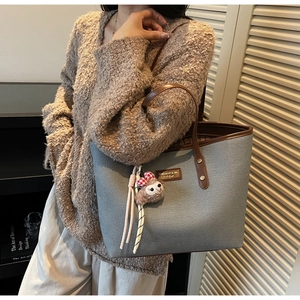Close-up of a large grey canvas tote bag with brown leather handles and plush animal charm
