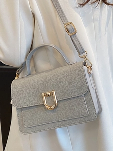 Gray lychee grain leather handbag with gold U-shaped buckle worn by a model in a white suit