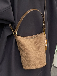Sac seau matelassé marron en faux daim, porté par un mannequin en trench-coat foncé
