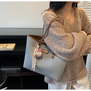 Detail of grey-blue tote bag with brown leather handles and a plush sheep charm accessory