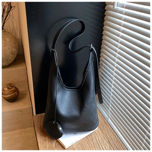Close-up of black litchi texture bucket bag with circular charm on a wooden surface