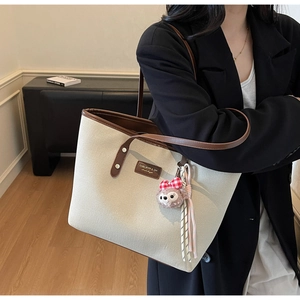Chic beige canvas tote bag with brown leather trim and cute plush charm shown on shoulder