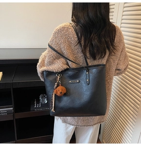 Detail of black leather tote bag featuring a cute teddy charm and metal logo plaque