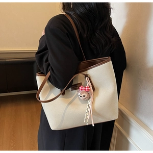 Detail of off-white canvas tote bag with brown leather trim and plush charm on the strap