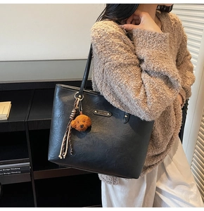 Close-up of black PU leather tote bag featuring a cute poodle plush charm and metal logo tag