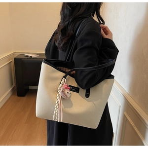 Close-up of off-white canvas tote bag with black leather trim and plush charm detail