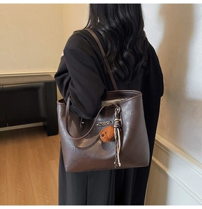 Detail of dark brown tote bag with bear charm pendant and metallic logo plate