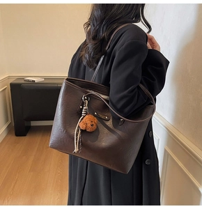 Close-up of brown faux leather tote bag with teddy bear charm and metal branding
