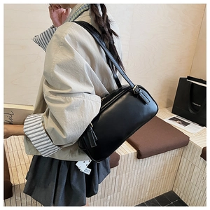 Close-up of black retro cylinder baguette bag with adjustable strap and metal buckle