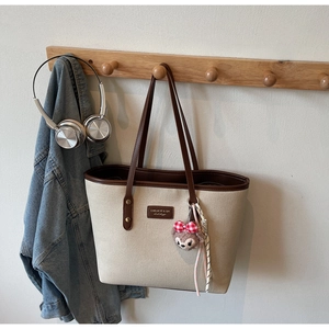 Detail of canvas tote bag with contrast leather trim, logo patch, and plush bear charm