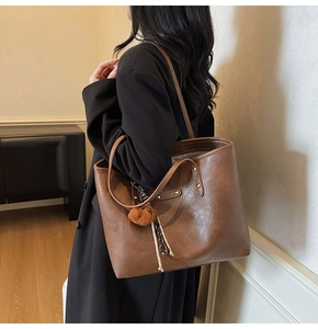 Macro detail of large brown tote bag with plush bear charm and woven cord detail