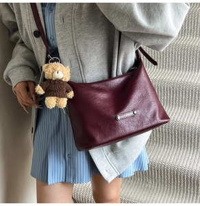 Close-up of burgundy hobo bag with teddy bear pendant and rectangular metal logo plate