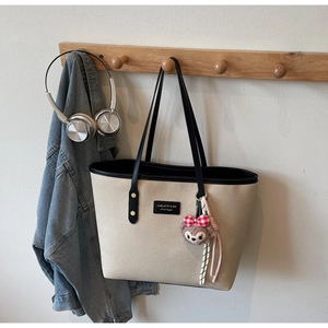 Detail of canvas tote bag with black leather trim, including a plush bear charm accessory