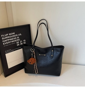 Detail of black PU leather tote bag with metallic logo and cute brown teddy bear pendant