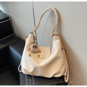 Detail of creamy white leather hobo bag with a soft plush sheep charm on a black book