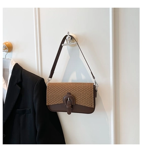 Detail of a brown woven texture and smooth leather flap with a decorative buckle strap