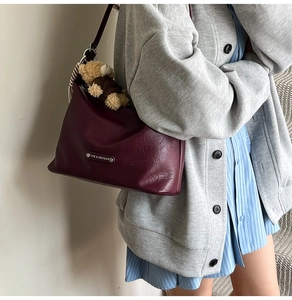 Detail of dark red tote bag with a cute bear pendant and silver fashion plate