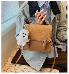 Close-up of brown quilted bag with retro buckles and cute white plush puppy charm