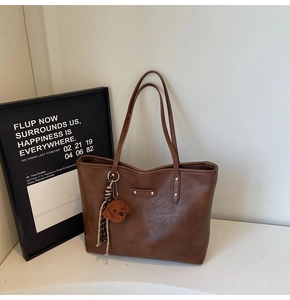 Close-up of brown leather tote bag featuring a gold brand plaque and a plush teddy bear charm
