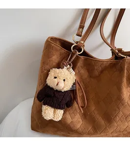 Cute beige plush bear charm with coffee knit sweater hanging on a textured brown tote bag