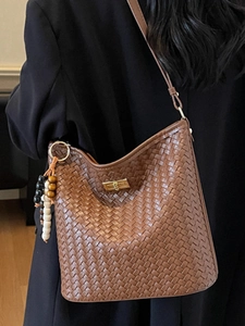 Brown woven bucket bag with golden twist lock and beaded tassel, worn by a model