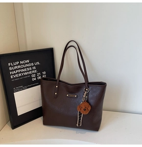 Detail of dark brown tote bag with leather texture and cute plush teddy bear charm