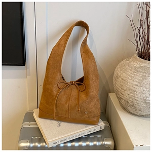Détail du sac hobo en daim caramel avec nœud en cuir et emblème en métal en forme de cœur