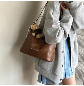 Detail view of brown vintage leather tote bag with a cute teddy bear plush charm