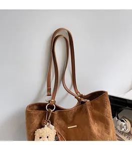 Detail of a large brown suede tote bag with diamond lattice pattern and a bear pendant