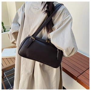 Detail of a vintage dark brown baguette bag with golden buckle and zipper on a shoulder