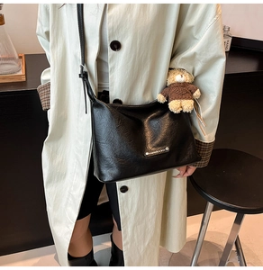 Detail of black soft leather hobo bag with teddy bear charm on cream trench coat