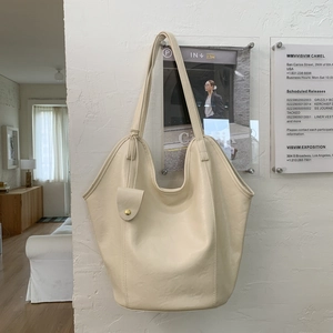 Détail d'un grand sac cabas en cuir blanc cassé suspendu sur un mur texturé chic