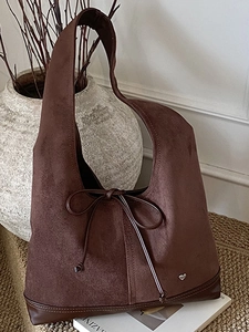 Sac cabas vintage en daim marron avec nœud en cuir et breloque cœur sur un bureau