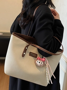 Chic beige canvas tote bag with brown leather handles and a plush bear charm detail