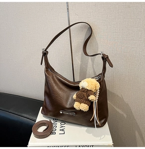 Detail view of brown PU leather tote with zipper, metal plaque, and cute bear charm accessory