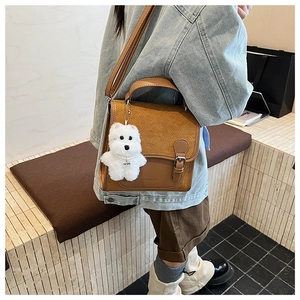 Detail of brown quilted leather bag with plush charm on a model in denim attire